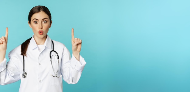 Free photo portrait of surprised young doctor female medical worker pointing fingers up gasping amazed showing