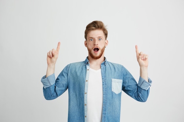 Portrait of surprised young handsome man with opened mouth pointing finger up.