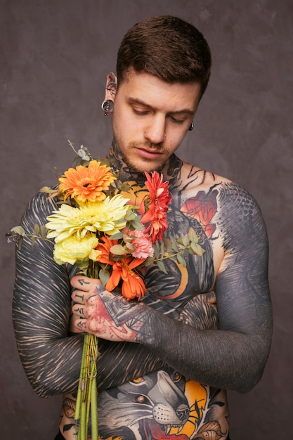 Free photo portrait of a tattooed hipster man holding bouquet in hand against gray background