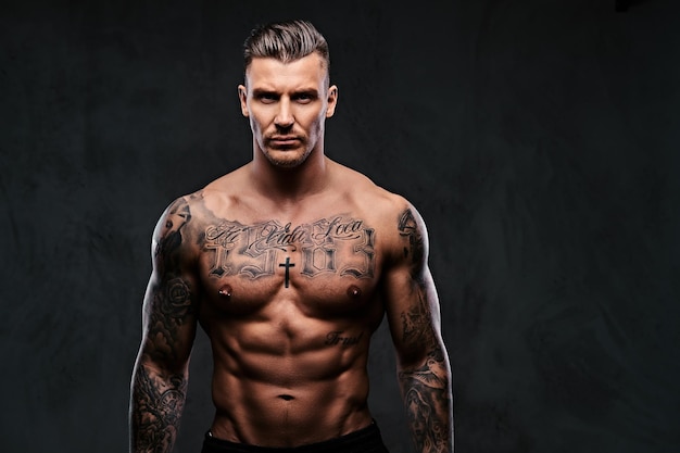 Free photo portrait of a tattooed muscular shirtless man with stylish hair posing at the camera on a dark background.