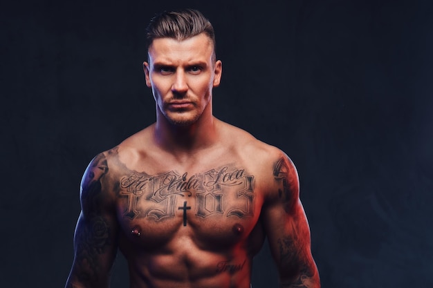 Free photo portrait of a tattooed muscular shirtless man with stylish hair posing at the camera on a dark background.