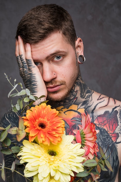 Portrait of a tattooed and pierced young man holding flowers in hand looking at camera