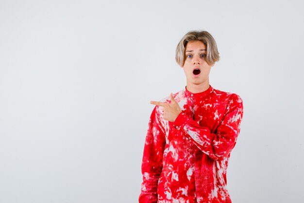 Portrait of teen blonde male pointing left in oversized shirt and looking scared front view