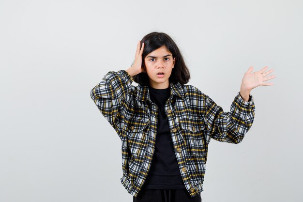 Portrait of teen girl holding hand on head, showing welcome gesture in casual shirt and looking shocked front view