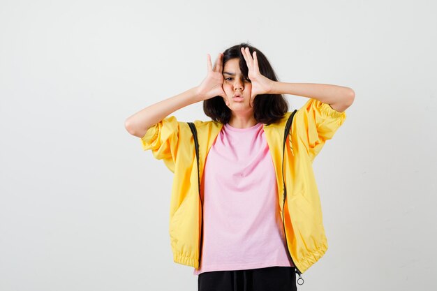 Portrait of teen girl holding hands on the both sides of face in t-shirt, jacket and looking annoyed front view