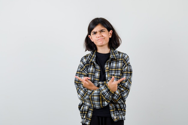 Portrait of teen girl pointing to opposite directions with crossed hands in casual shirt and looking indecisive front view