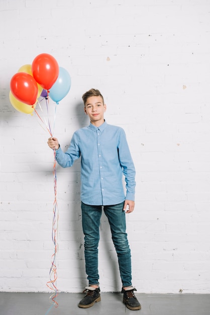 Free Photo portrait of teenage boy holding colorful balloons in hand