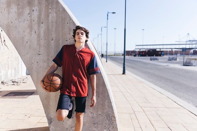 Free Photo portrait of a teenage boy leaning on wall with basketball