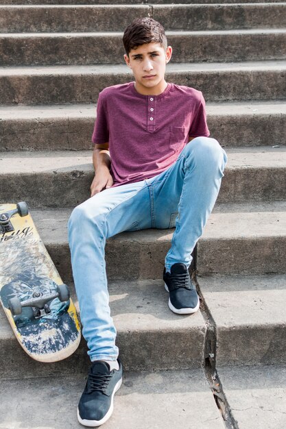 Portrait of a teenage boy sitting on concrete staircase with skateboard