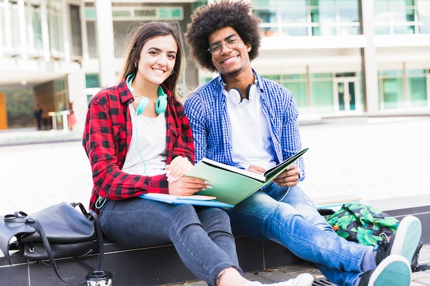 Portrait of teenage male and female students holding books in hand sitting at campus