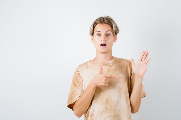 Portrait of teenager boy pointing at raised hand in t-shirt and looking puzzled front view