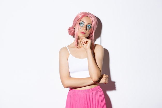 Free photo portrait of thoughtful attractive female model with pink anime wig and bright makeup, looking at upper left corner banner and thinking, making choice, standing.