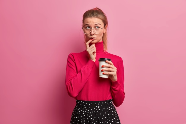 Free photo portrait of thoughtful beautiful teenage european girl concentrated above holds disposable cup of coffee