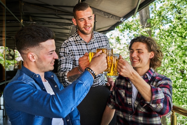 Portrait of three male friends drinking beer in pub.