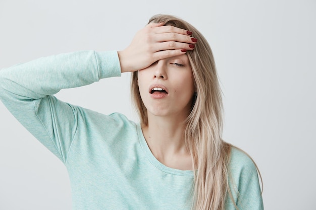 Portrait of tired exhausted blonde young female has terrible headache after work, comes home in bad mood, being fed up with everything