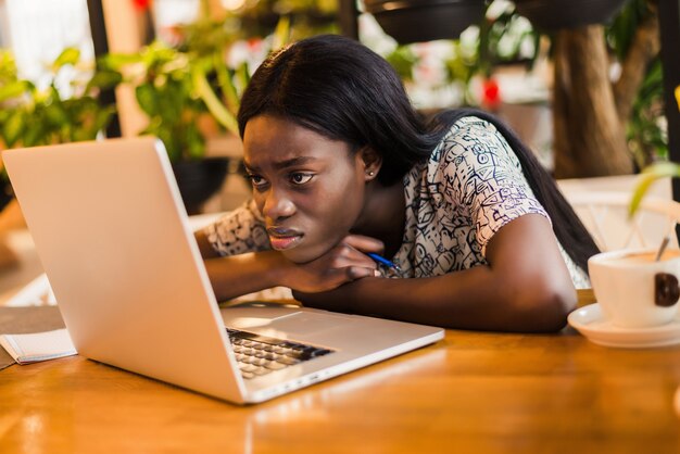 Portrait of a tired young african woman sitting at the table with laptop computer while sleeping at a cafe