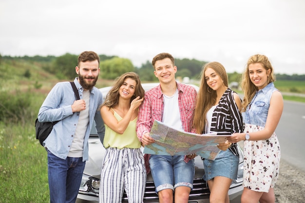 Portrait of tourist friends holding map standing in front of car at outdoors