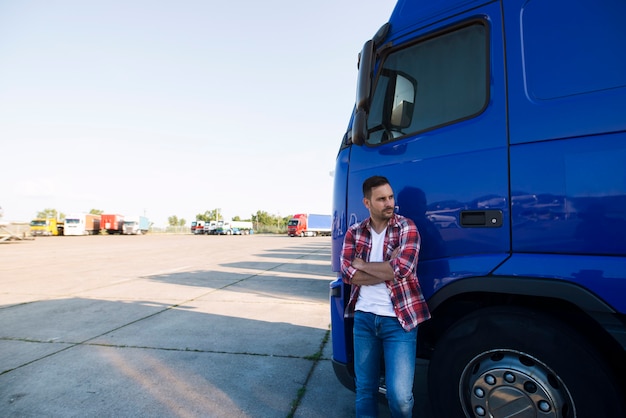 Portrait of trucker in casual clothes standing by his truck vehicle and looking sideways