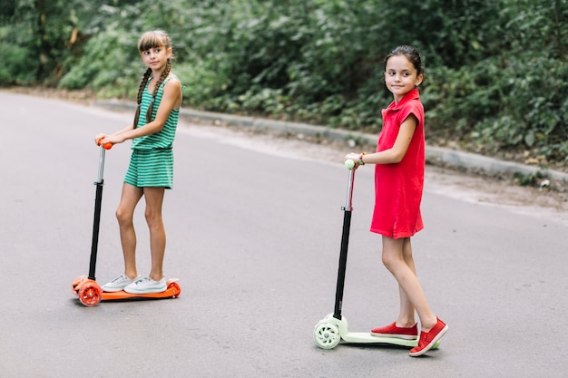 Portrait of two girls standing over push scooter on street