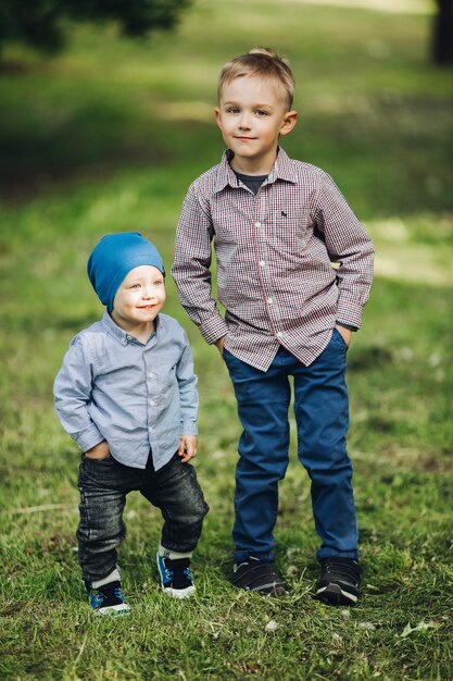 Portrait of two little boys wearing in casual looks posing in park holding hands in pockets Handsome brothers walking and playing together Concept of fashionable and stylish kids look of clothes