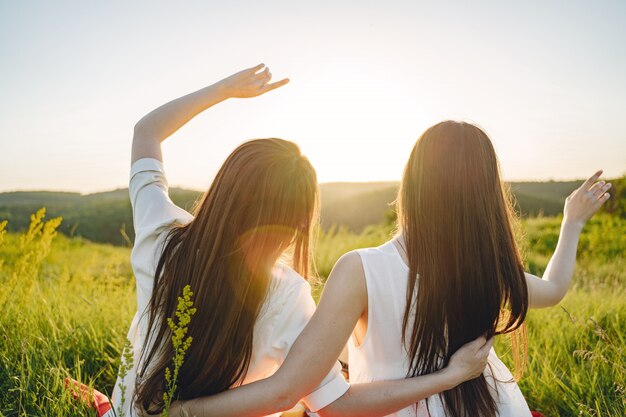 Portrait of two sisters in white dresses with long hair in a field