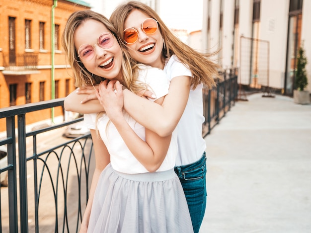 Free Photo portrait of two young beautiful blond smiling hipster girls in trendy summer white t-shirt clothes.   . positive models having fun in sunglasses.hugging