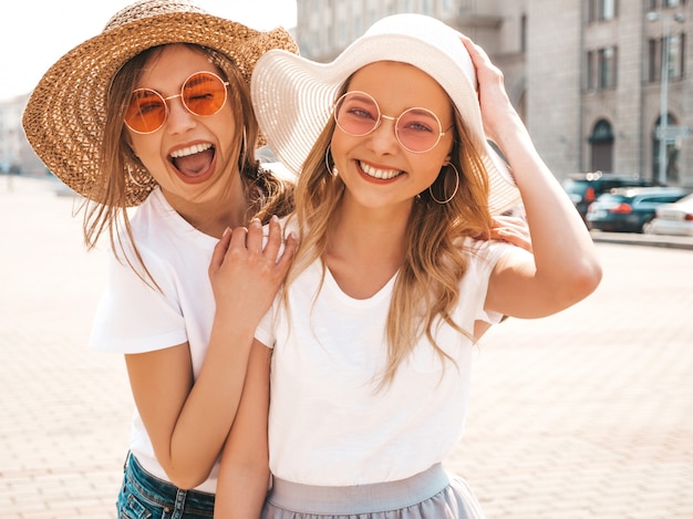 Portrait of two young beautiful blond smiling hipster girls in trendy summer white t-shirt clothes.  