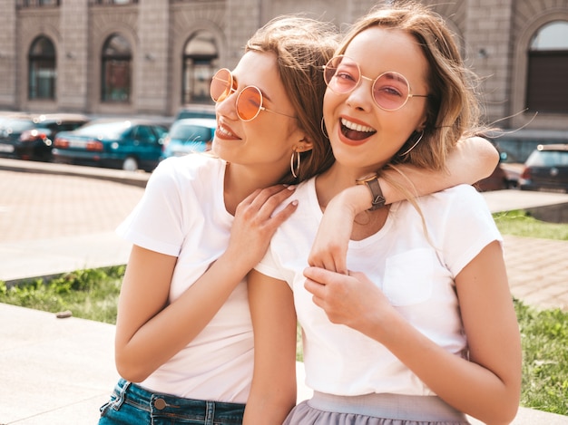 Portrait of two young beautiful blond smiling hipster girls in trendy summer white t-shirt clothes.  