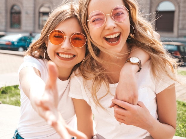 Portrait of two young beautiful blond smiling hipster girls in trendy summer white t-shirt clothes.  