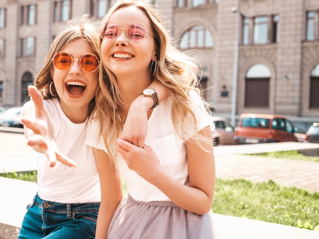 Free photo portrait of two young beautiful blond smiling hipster girls in trendy summer white t-shirt clothes.