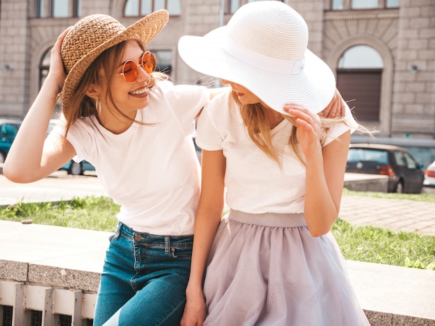 Free photo portrait of two young beautiful blond smiling hipster girls in trendy summer white t-shirt clothes.