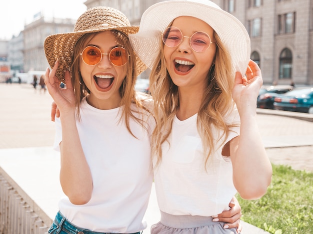 Free photo portrait of two young beautiful blond smiling hipster girls in trendy summer white t-shirt clothes.