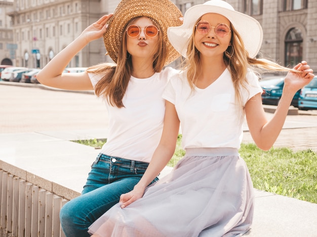 Portrait of two young beautiful blond smiling hipster girls in trendy summer white t-shirt clothes.  . 