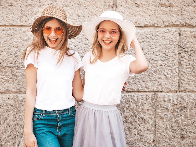 Portrait of two young beautiful blond smiling hipster girls in trendy summer white t-shirt clothes.  . 