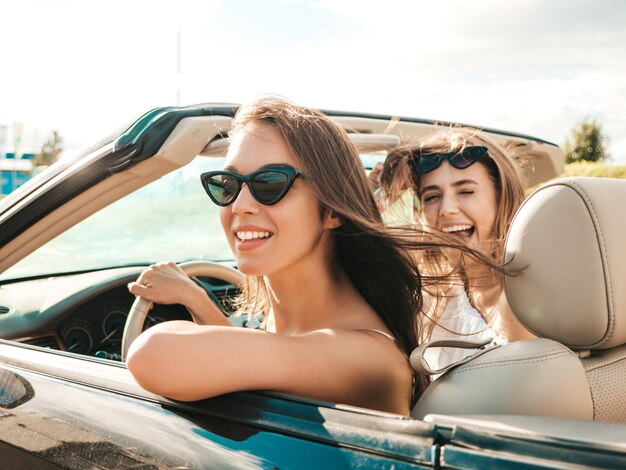 Portrait of two young beautiful and smiling hipster female in convertible car