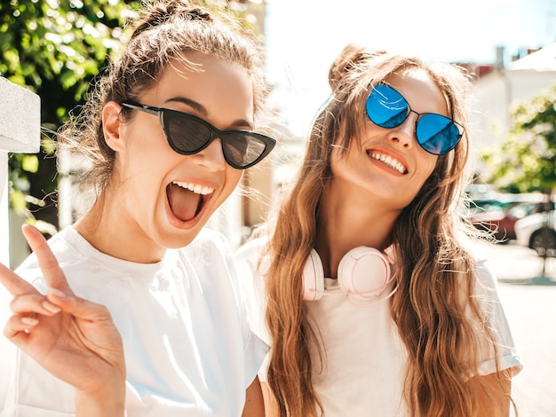 Portrait of two young beautiful smiling hipster female in trendy summer white t-shirt clothes