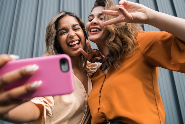 Free Photo portrait of two young friends having fun together and taking a selfie with a mobile phone outdoors