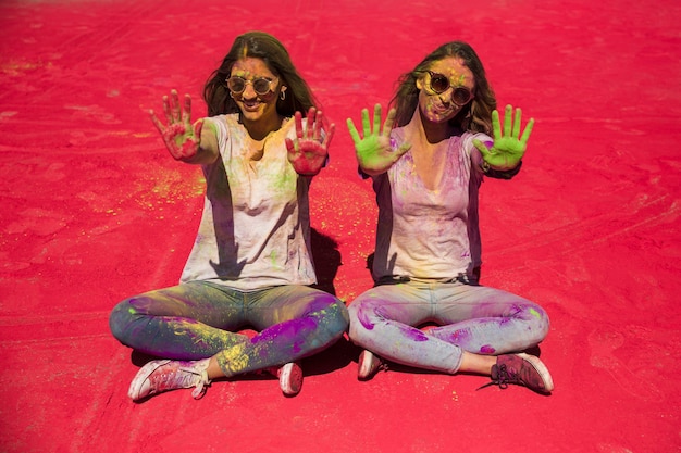 Free Photo portrait of two young women showing their palms painted with holi color