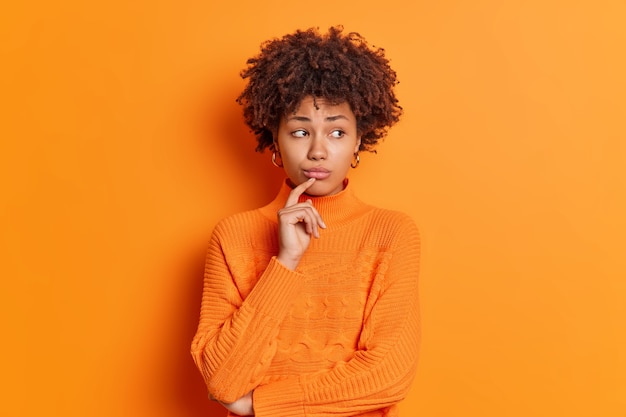 Free photo portrait of unhappy thoughtful melancholy young woman feels upset looks aside with displeased expression thinks how to solve problem isolated over orange wall