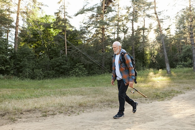 Free Photo portrait of unshaven bald european male pensioner with backpack, carrying fishery rod or spinning reel, going to catch fish on river bank. recreation fishing, active healthy lifestyle and leisure