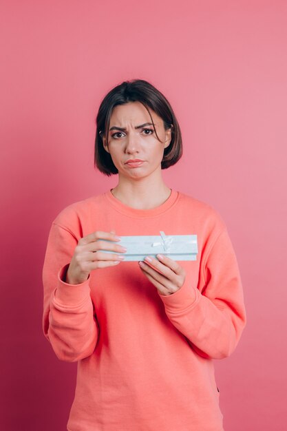 Portrait of upset frustrated girl opening gift box isolated on pink background