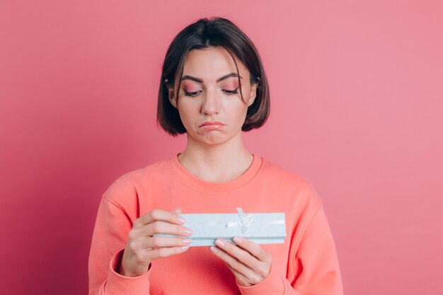 Portrait of upset frustrated girl opening gift box isolated on pink background