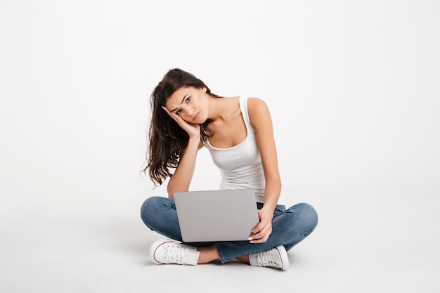 Portrait of an upset woman dressed in tank-top holding laptop