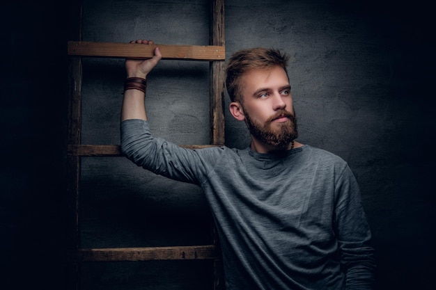 Free Photo portrait of an urban bearded male posing near old vintage ladder on grey background.