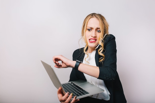 Portrait very busy young businesswoman in formal suit with laptop talking on phone, looking at watch. Being late, job, managment, meetings, working, profession