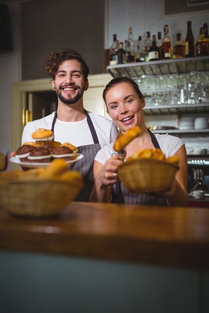 Portrait of waiter and waitress holding cupcakes and bread