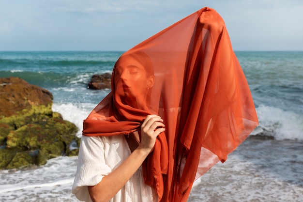 Free photo portrait of woman at the beach covering her face with veil