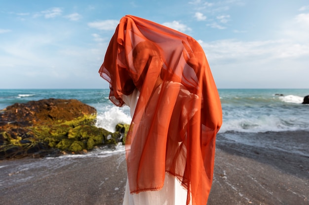 Free photo portrait of woman at the beach covering her face with veil