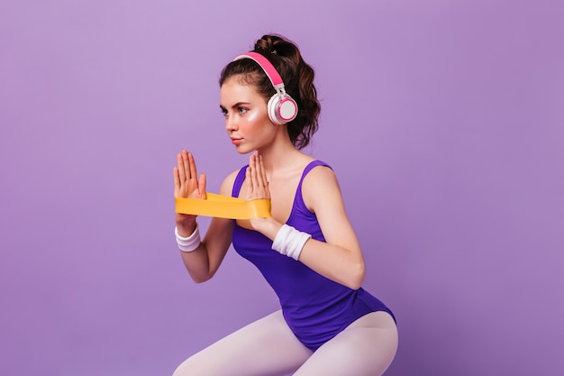 Portrait of woman in bodysuit and leggings doing squats with elastic band