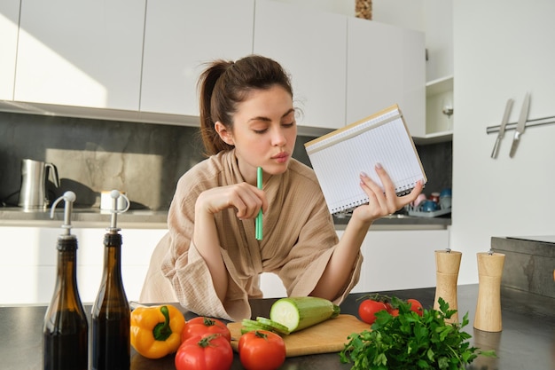 Free photo portrait of woman checking grocery list looking at vegetables holding notebook reading recipe while